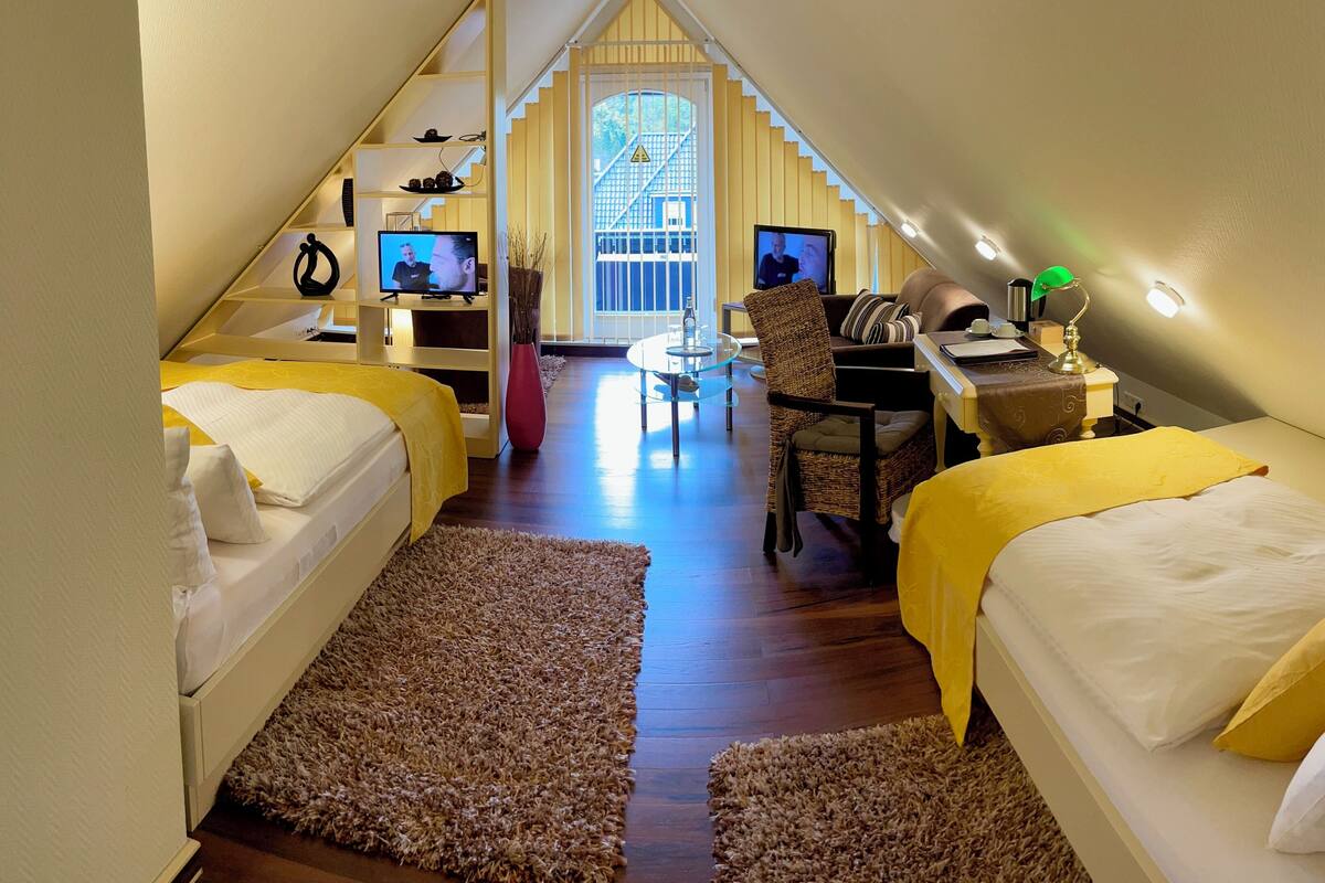 A cozy attic bedroom with two beds, a desk, and a TV.