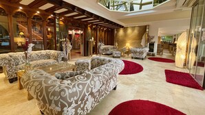 A spacious lobby with patterned sofas, a red carpet, and a high ceiling with natural light. - Villa am Park (Bad Zwischenahn)