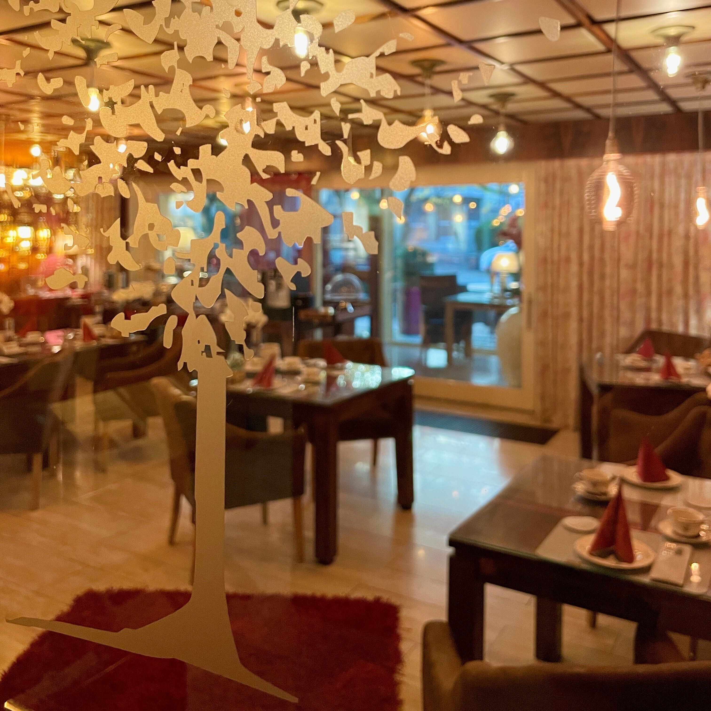 A restaurant interior with a decorative tree centerpiece, dining tables, chairs, and hanging lights.