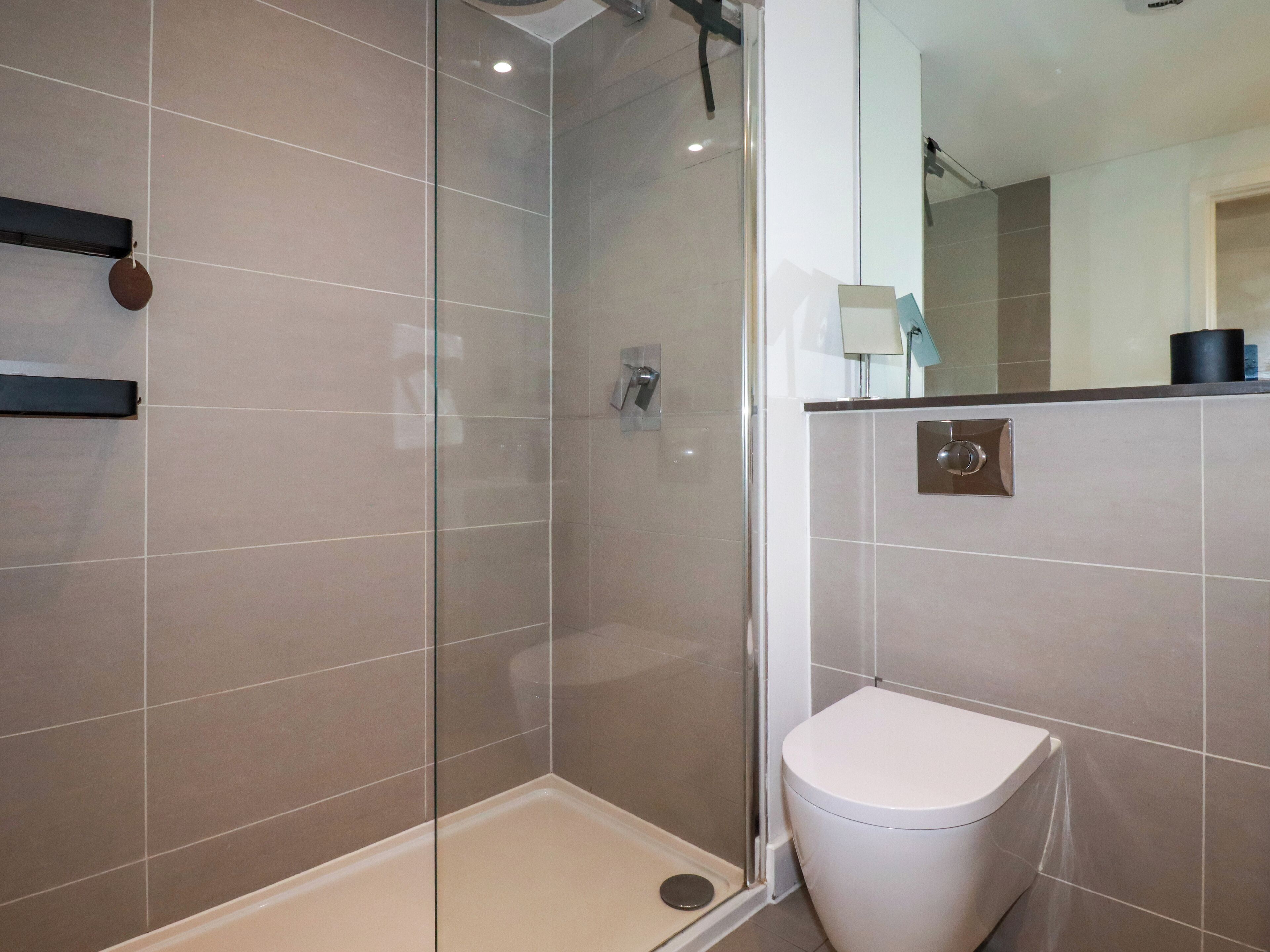 A modern bathroom with a glass-enclosed shower, a white toilet, and a mirror above the sink.