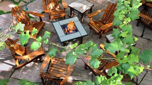Een rond zitgedeelte buiten met houten stoelen en een vuurkorf in het midden.