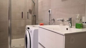 Un baño moderno con cabina de ducha de vidrio, lavadora integrada, lavamanos con dispensador de jabón y un espejo sobre el lavamanos.