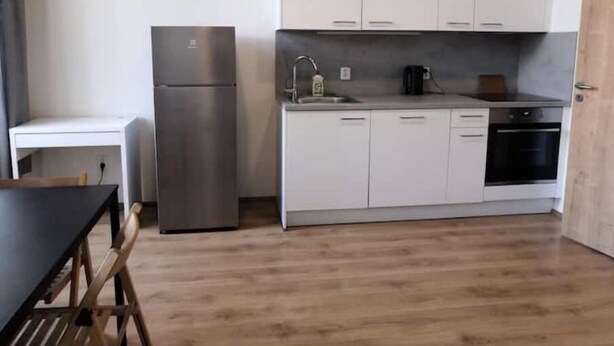 Una cocina compacta con armarios blancos, un refrigerador de acero inoxidable, un fregadero y una estufa.