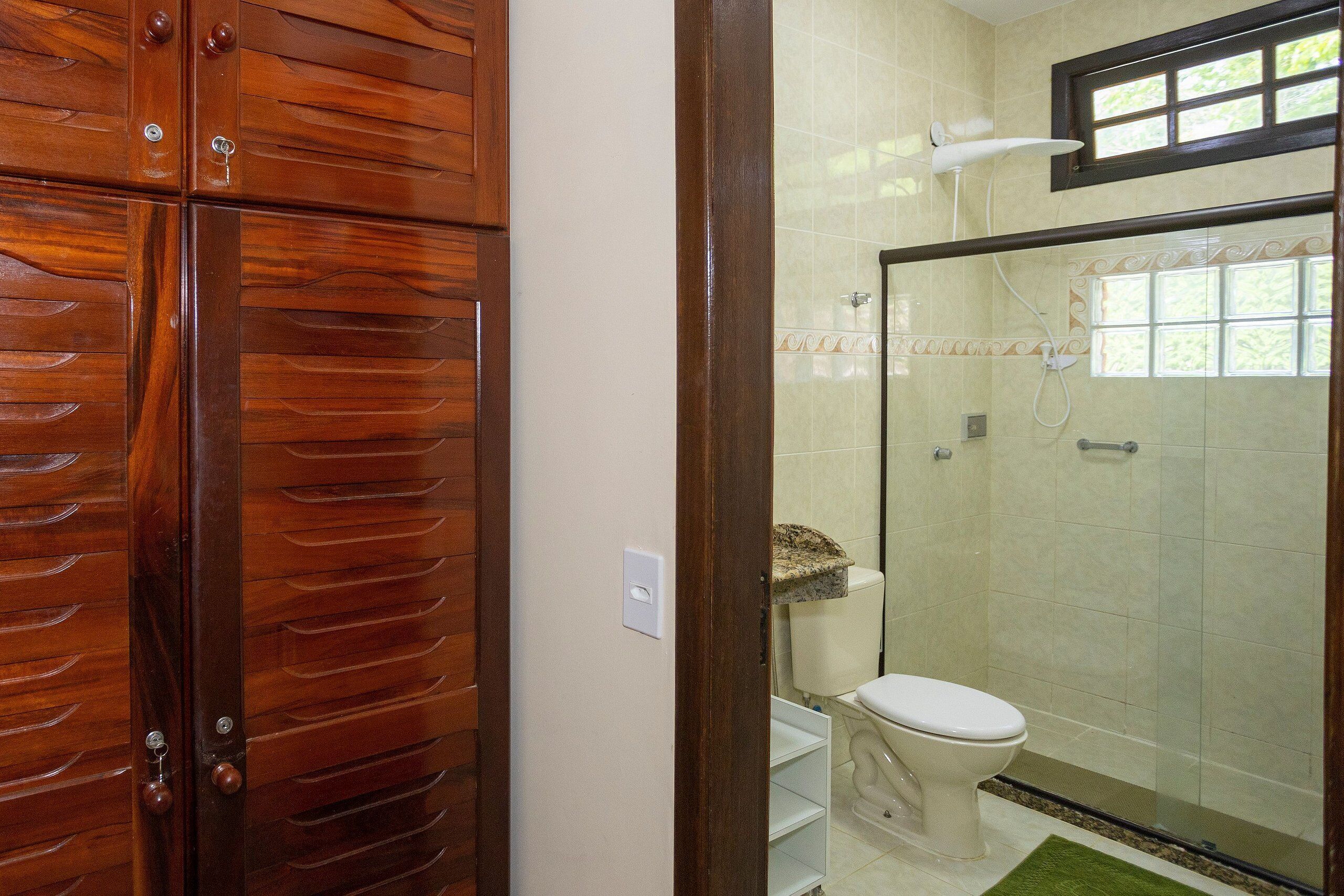 A bathroom with a wooden door, a toilet, a shower, and a tiled wall.