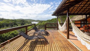 A wooden deck with two chairs and a hammock, overlooking a lush landscape with a river and hills. - Bz19 Casa 200m da Praia da Ferradura (Buzios)