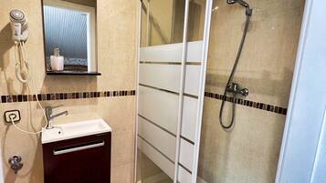 Ein Badezimmer mit Duschkabine, Waschbecken mit Spiegel darüber und einem an der Wand montierten Fön.