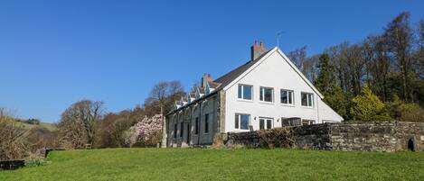 A white two-story house with a stone wall and a grassy lawn.