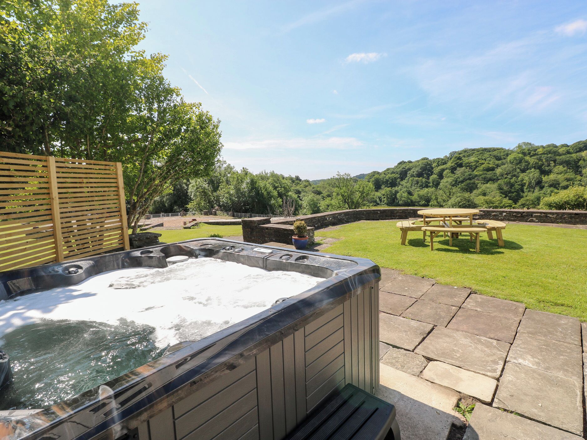 Un bain à remous avec une terrasse en pierre, une clôture en bois et une table de pique-nique, le tout aménagé dans un jardin.