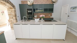 A modern kitchen with a large island, built-in appliances, and pendant lighting. - Coytrahen House (Bridgend)