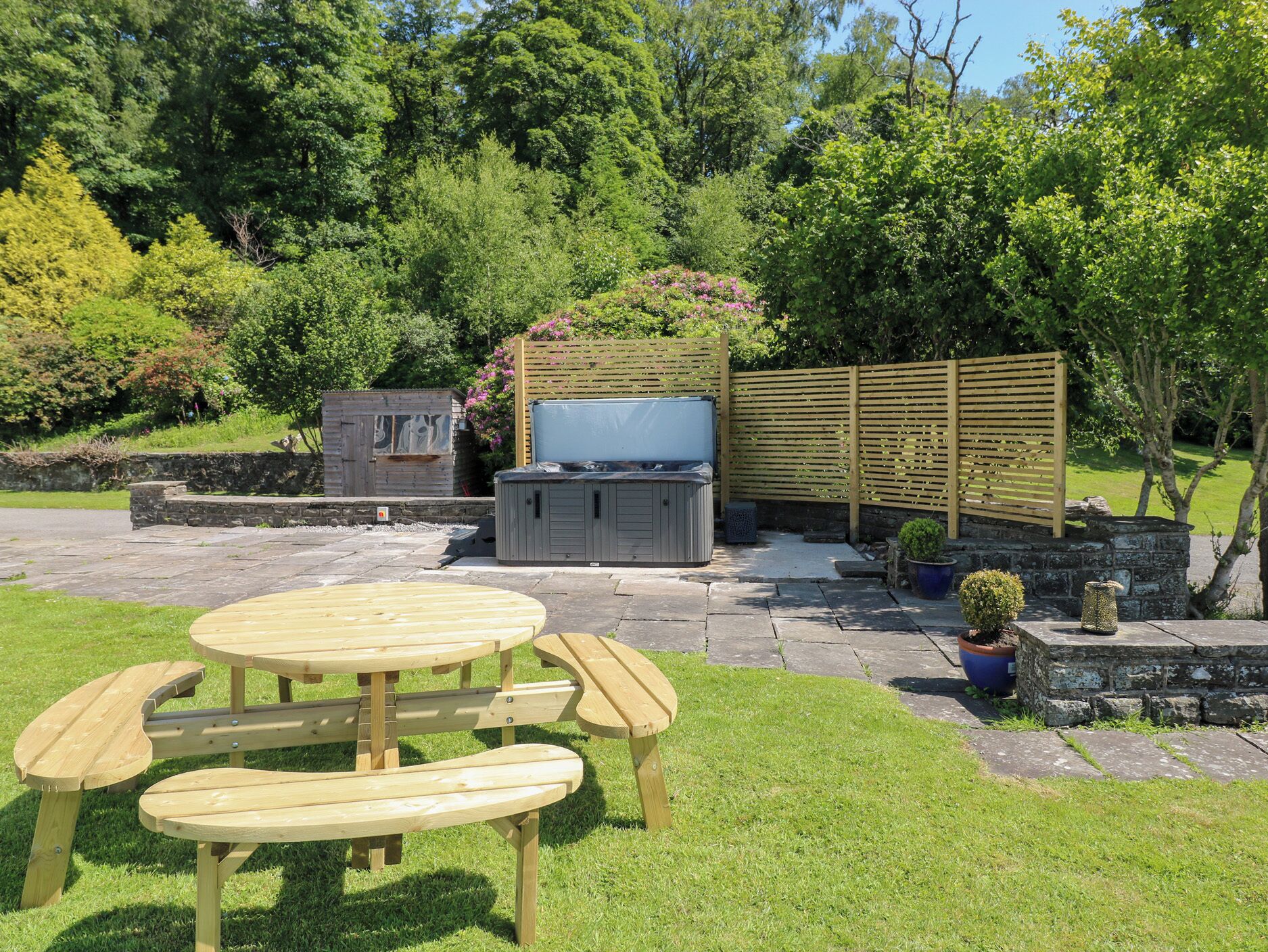 A patio with a wooden table and benches, a hot tub, and a wooden fence.