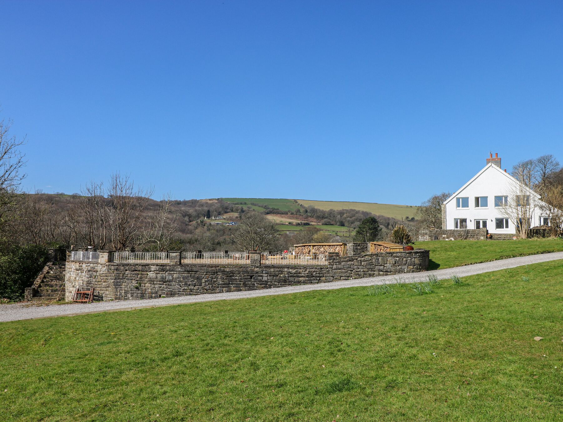 Una casa blanca con un muro de piedra y un camino de grava en un entorno rural.