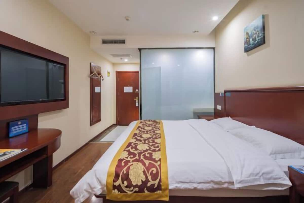 Habitación de hotel con cama, escritorio, televisor y puerta que da a un baño.