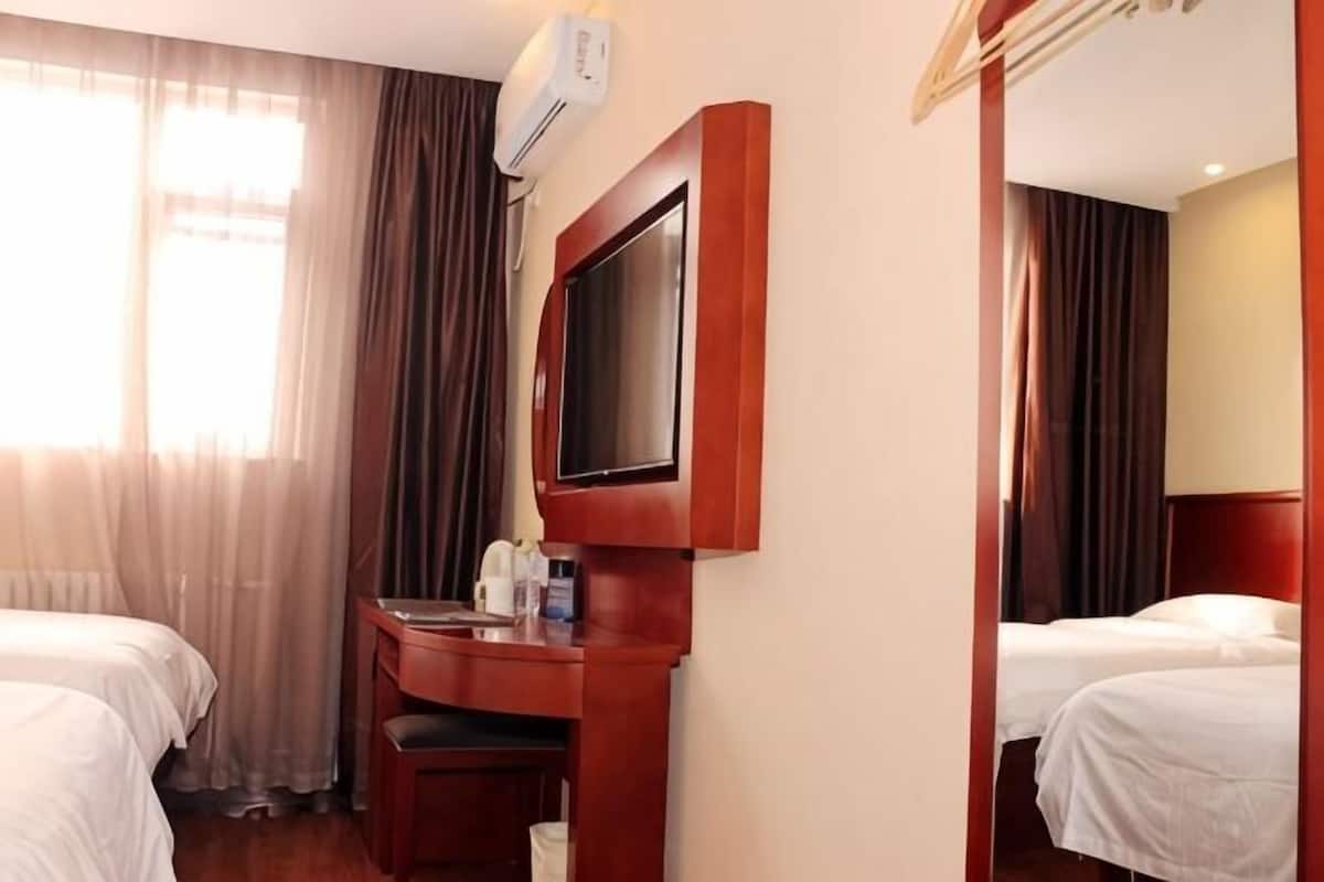 Una habitación de hotel con dos camas, un escritorio con silla, un televisor y un espejo.