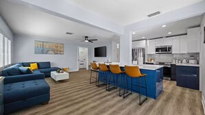 Ein modernes Wohnzimmer mit einem blauen Sofa, einem Couchtisch und einer Küchenzeile mit Bar und Hockern.