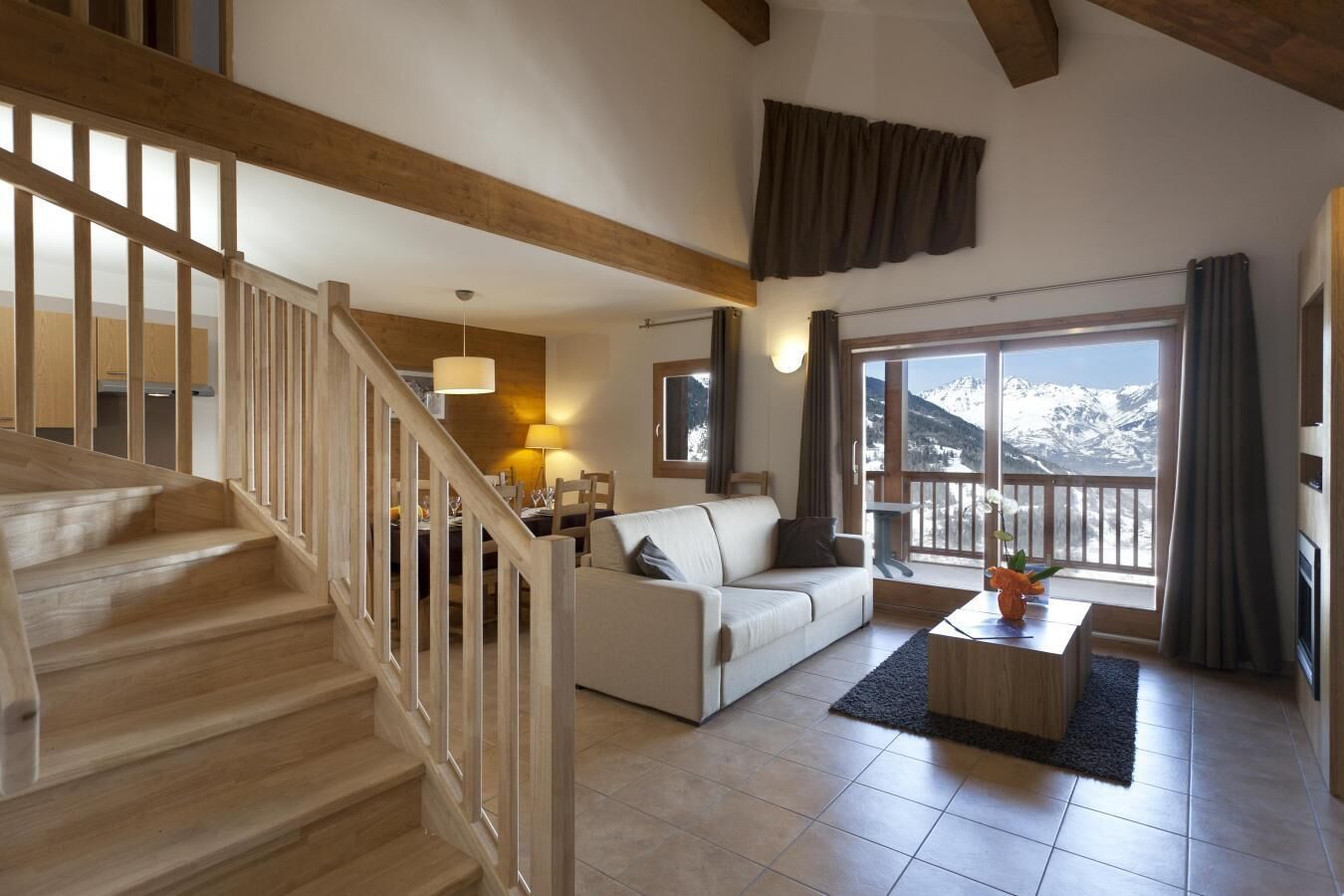 Un vaste espace de vie comprenant un escalier, un canapé blanc, une table à manger et une vue sur des montagnes enneigées.