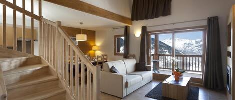 Un vaste espace de vie comprenant un escalier, un canapé blanc, une table à manger et une vue sur des montagnes enneigées.