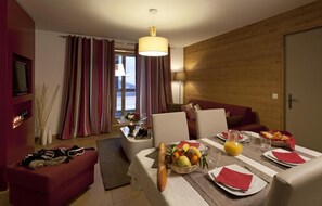 A modern hotel room with a dining area, a sofa, and a wooden accent wall.