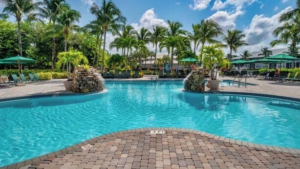 Une piscine entourée de palmiers et de chaises longues, avec une terrasse en briques.