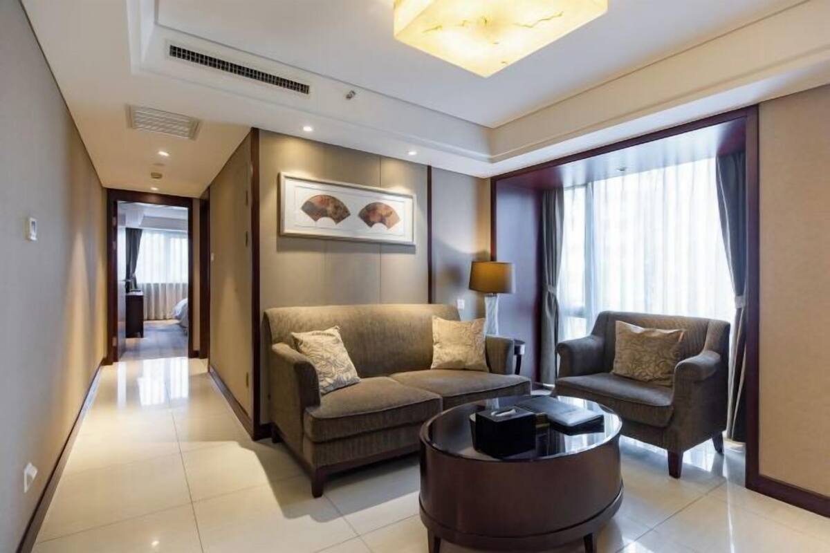 Ein modernes Hotelzimmer mit einer Sofagarnitur, einem Couchtisch und einem großen Fenster mit Vorhängen.