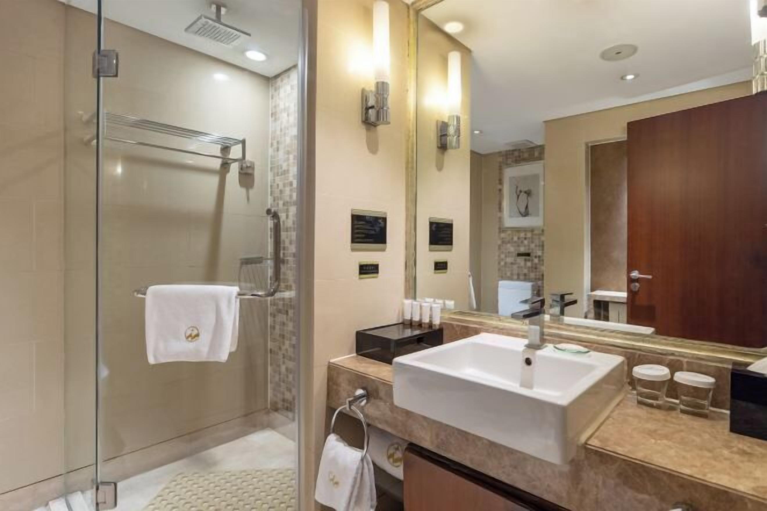 A modern bathroom with a glass-enclosed shower, a large mirror, and a white sink.