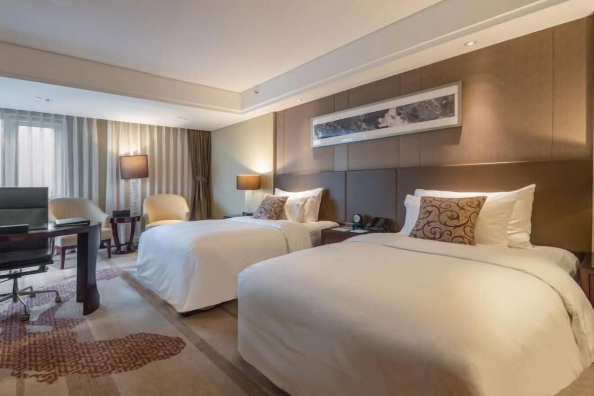 Ein Hotelzimmer mit zwei Betten, einem Schreibtisch, einem Stuhl, einem Fernseher und einer Lampe.