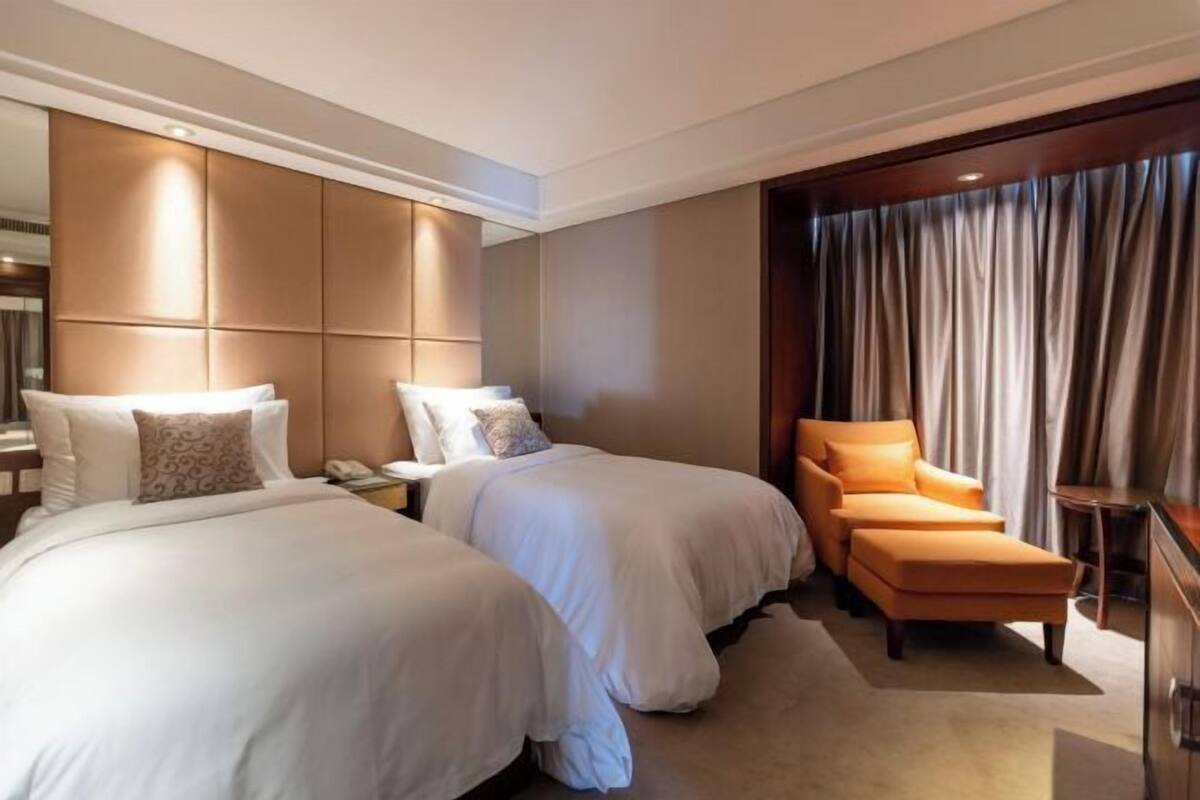 Ein Hotelzimmer mit zwei Betten, einem Sofa, einem Schreibtisch und einem großen Fenster mit Vorhängen.