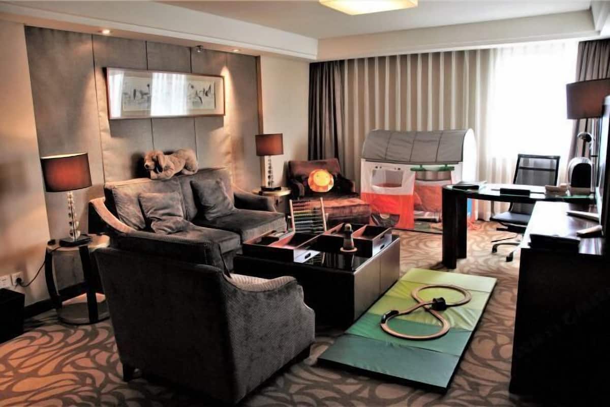 Ein Hotelzimmer mit einer Couch, Sesseln, einem Schreibtisch, einem Laptop und einem Laufband mit passender Matte.