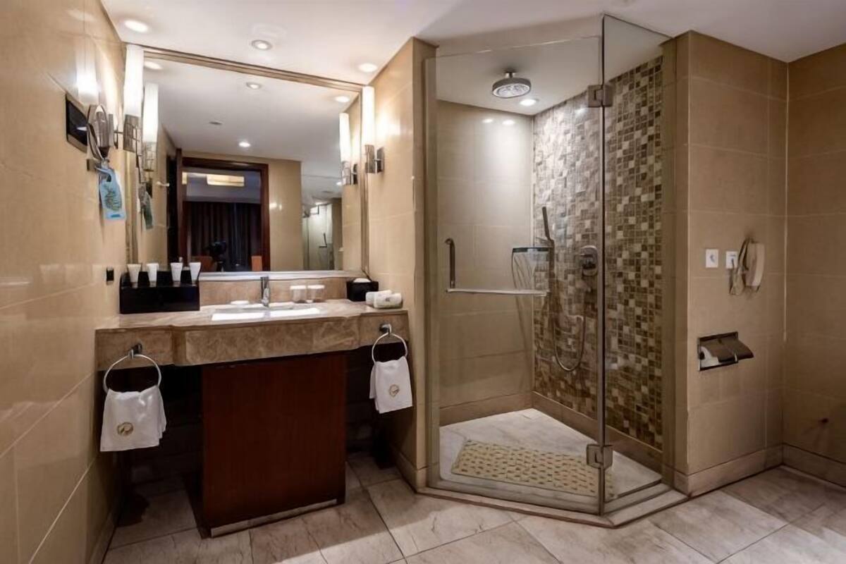 Ein modernes Badezimmer mit einer Glaskabine zur Dusche, einem Waschbecken mit Spiegel und einem gefliesten Boden.