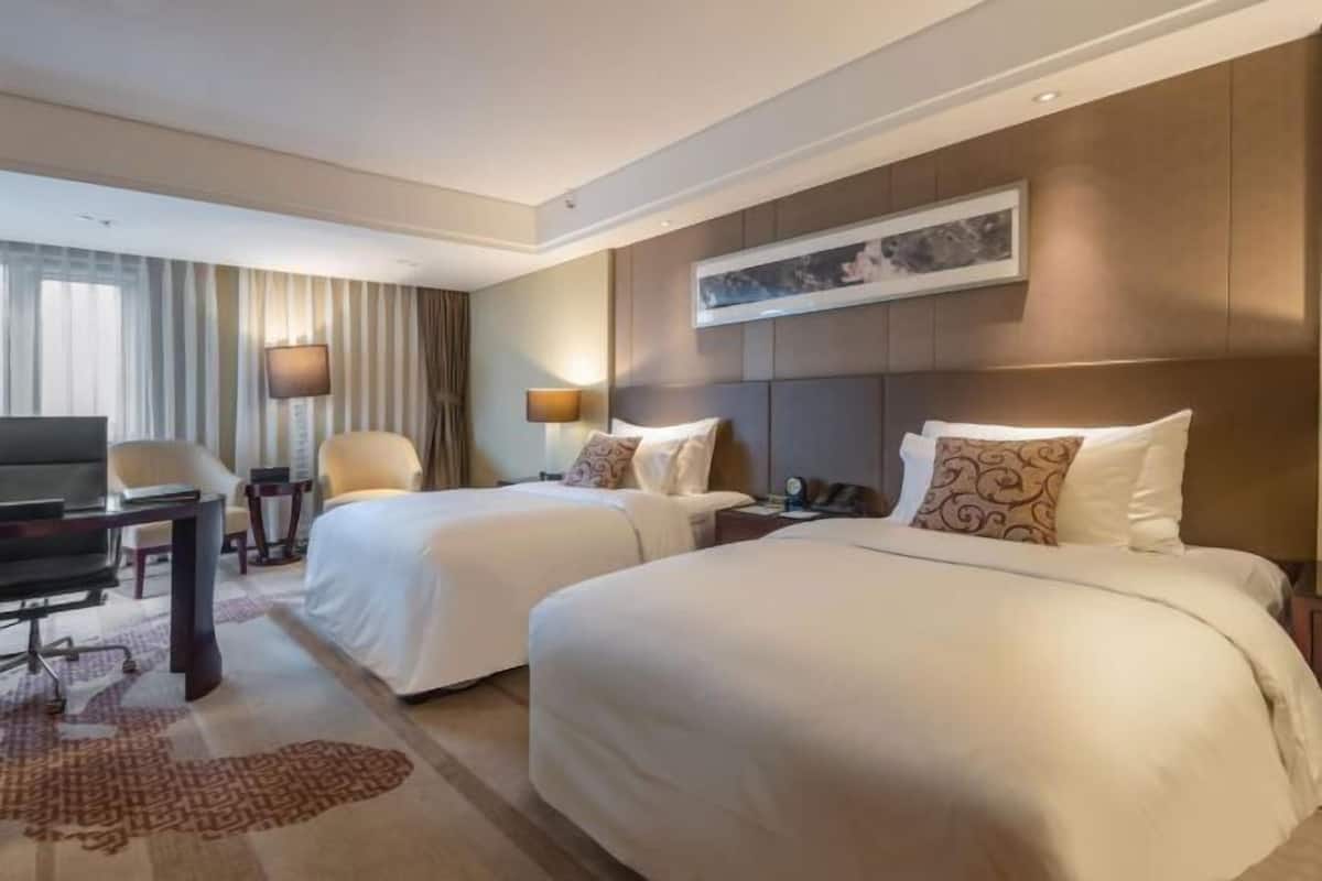Ein Hotelzimmer mit zwei Betten, einem Schreibtisch, einem Stuhl, einem Fernseher und einem Bild an der Wand.