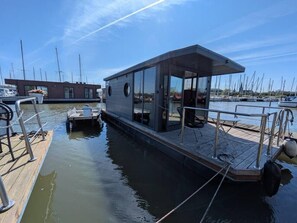 Un moderno cobertizo para botes con un muelle techado, un ventanal pequeño y un embarcadero que se adentra en aguas tranquilas.