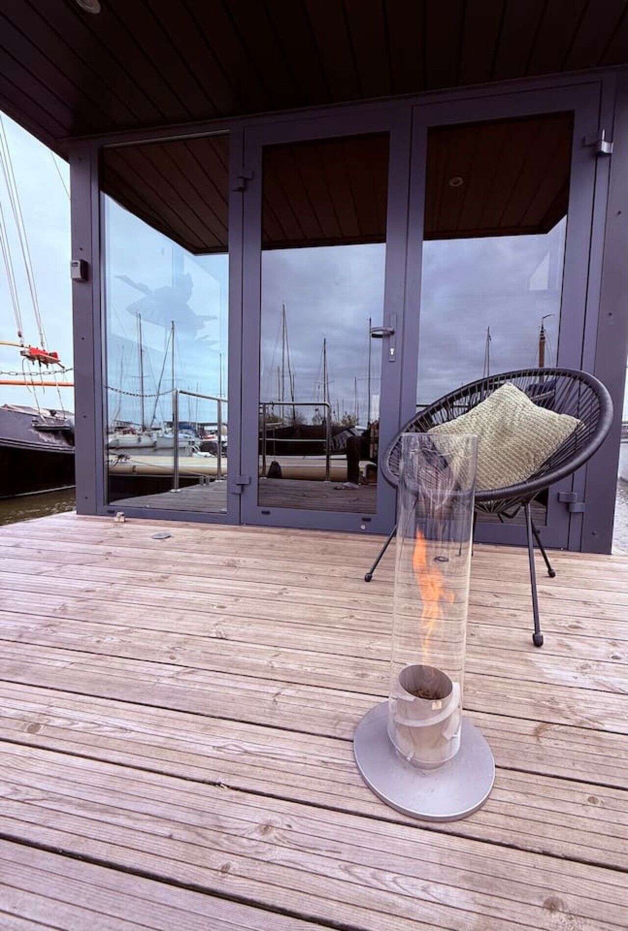 Eine Holzterrasse mit einem Glastisch und einem Stuhl mit Blick auf eine Marina und Boote.