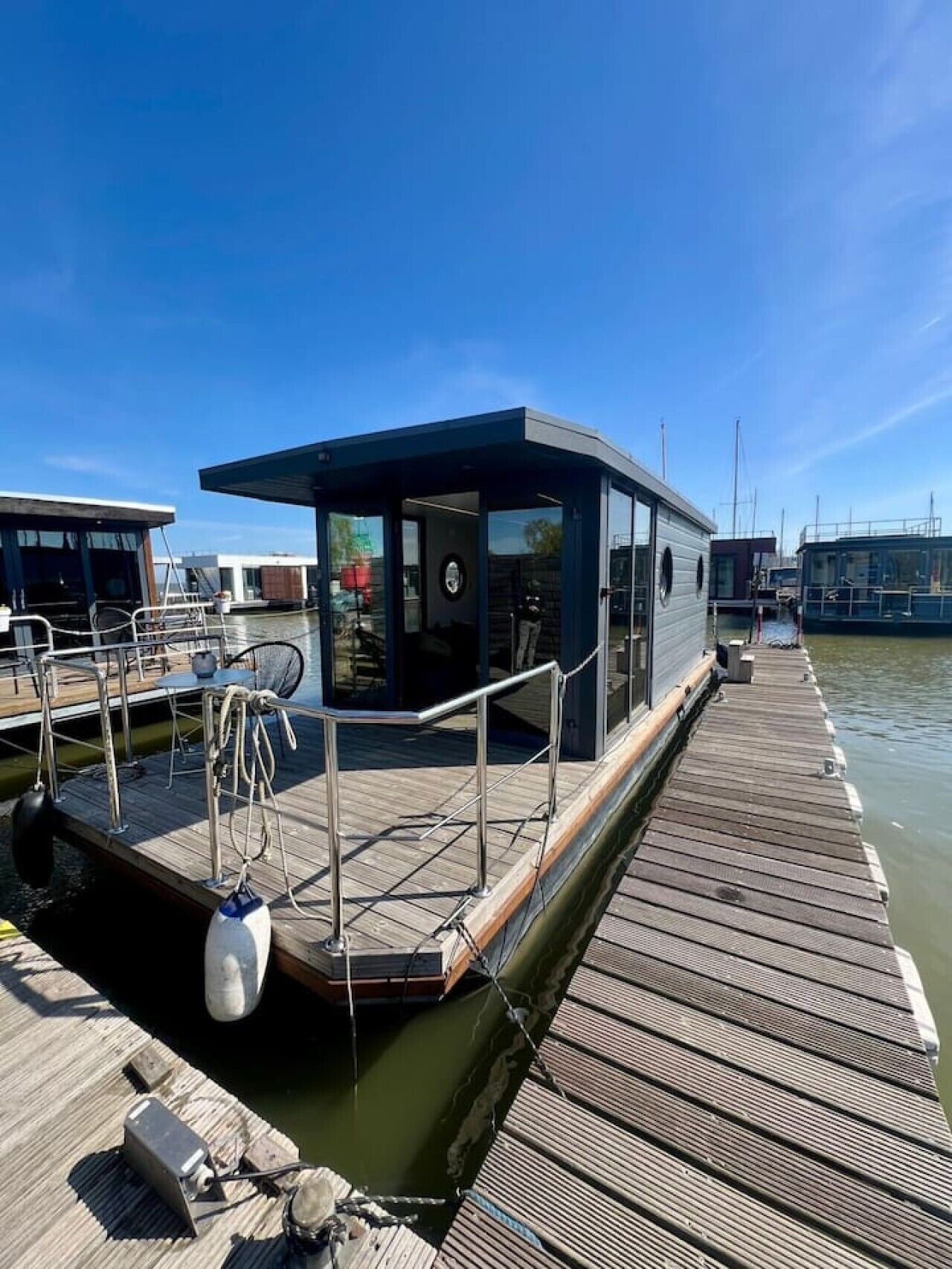 A modern boat docked at a pier with a covered seating area and a small building.