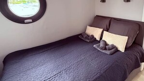 A single bed with a dark blue quilt, a round window with a view of the outside, and two wall-mounted light fixtures. - Cosy Houseboat `Eclipse` in Marina Monnickendam (Monnickendam)