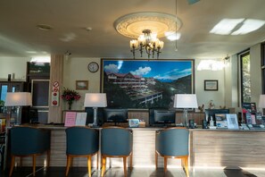 A hotel reception area with a large window, a chandelier, a clock, and a desk with computers and chairs.