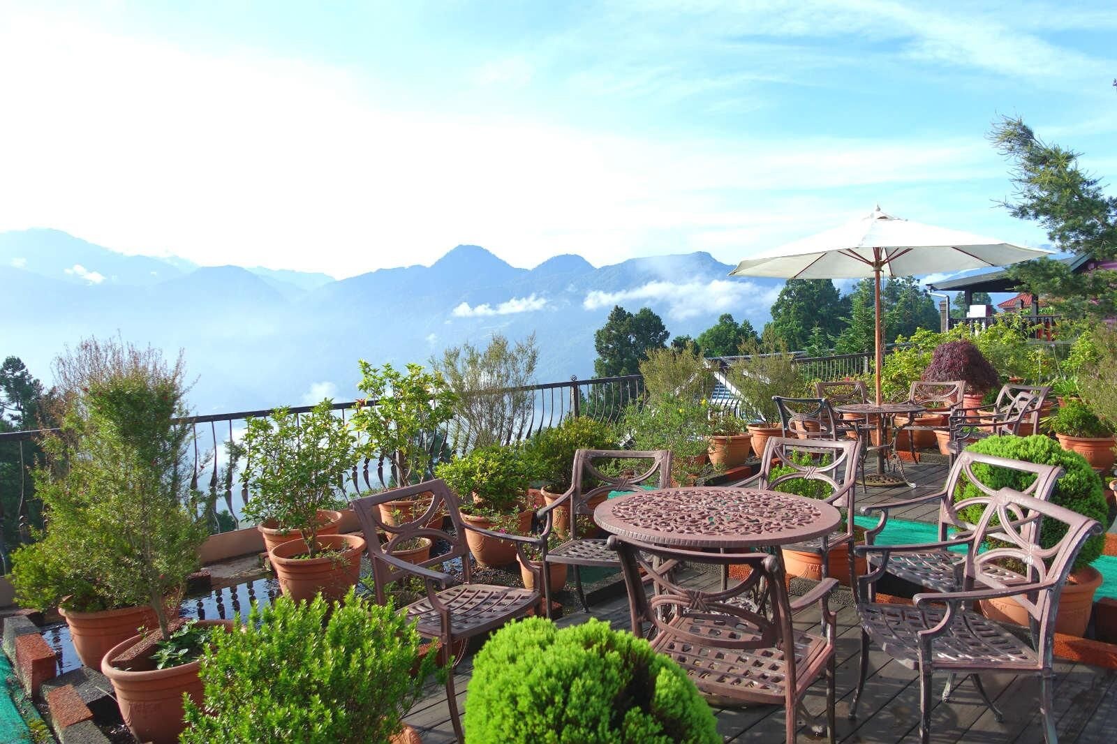Un patio exterior con asientos y plantas en macetas, con vistas a un paisaje montañoso.
