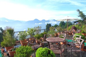 An outdoor patio with seating and potted plants, overlooking a mountainous landscape.