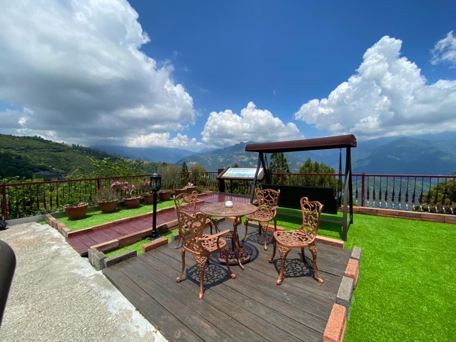 A deck with a table and chairs, surrounded by potted plants and a view of a mountainous landscape.