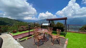 A deck with a table and chairs, surrounded by potted plants and a view of a mountainous landscape.