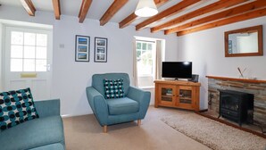 A living room with a blue sofa, a television, a fireplace, and wooden beams on the ceiling. - Pennine (Truro)