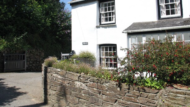 A two-story white house with a stone wall in front, a stone gate, and a large tree to the left. - Pennine (Truro)