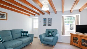 A living room with a blue sofa, a blue armchair, and a wooden cabinet with a television. - Pennine (Truro)