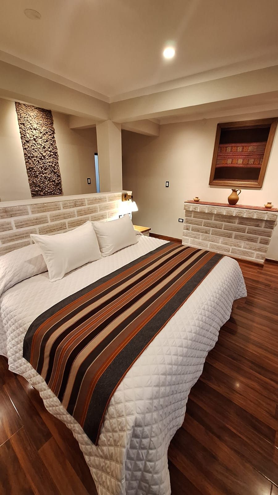 A bedroom with a large bed, a stone accent wall, a fireplace, and a window with curtains.