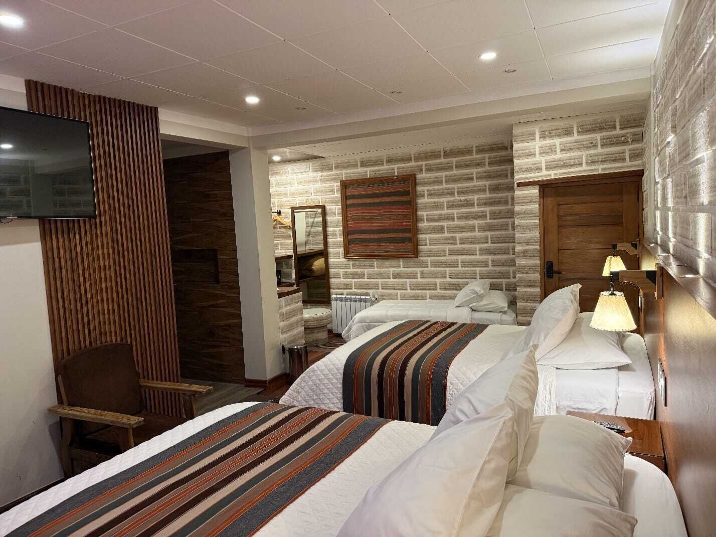 A hotel room with two beds, a TV, a wooden accent wall, a mirror, and a lamp.