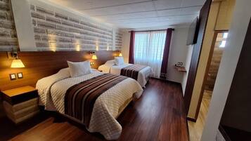 Habitación de hotel con dos camas, cabeceros de madera y una pared con diseño de ladrillo.