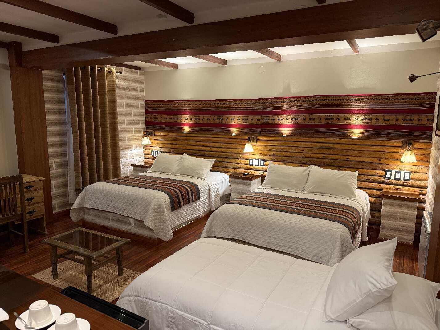 Una habitación de hotel con dos camas, un cabecero de madera, una mesita y una ventana con cortinas.