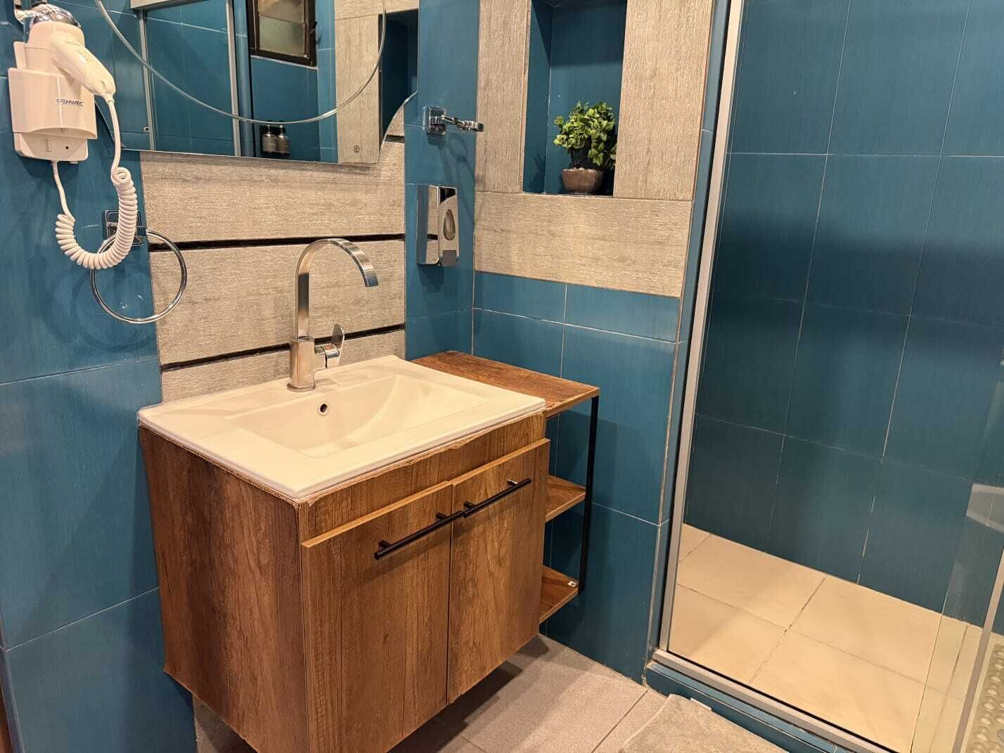 Een badkamer met een houten wastafelmeubel, een witte wastafel, een spiegel en een blauwe betegelde muur.