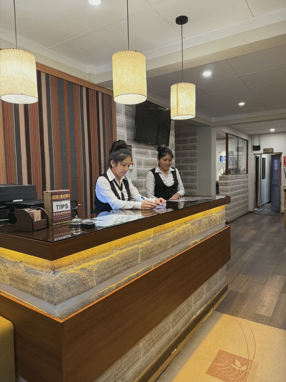 Una mesa de recepción con dos empleados, un letrero que dice 'TIPS' y un cartel de 'COSTA CAFE' al fondo.