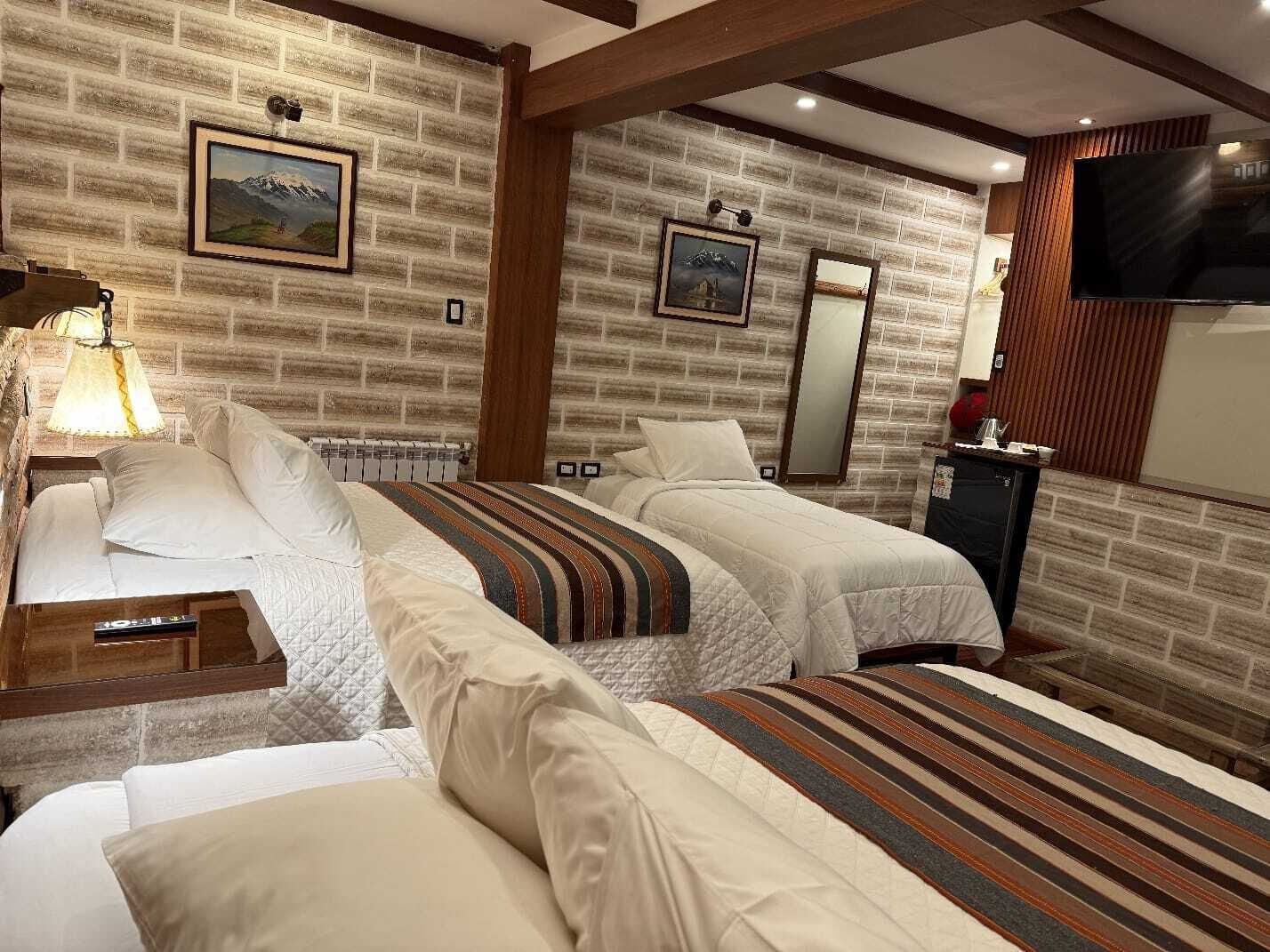Habitación de hotel con pared de ladrillo, dos camas, un televisor y un armario de madera.