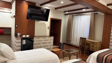A hotel room with two beds, a TV mounted on the wall, a small table, and a wooden bench.