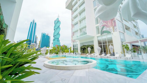 Zona de piscina moderna de hotel con un jacuzzi circular, sillones de descanso y vistas al horizonte de la ciudad.